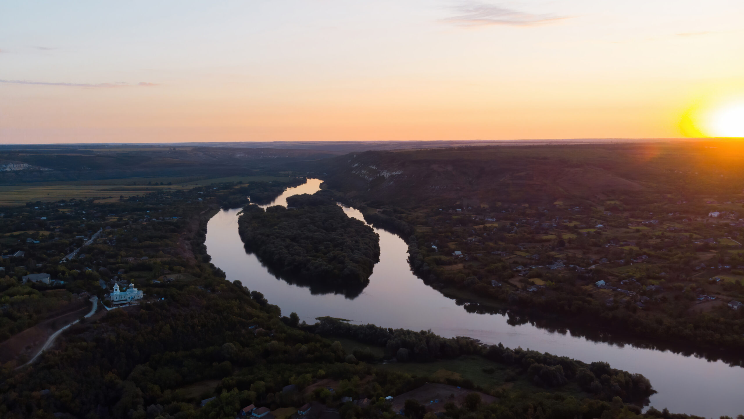Sunrise in Moldova, village with orthodox church, river dividing into two parts, hills and fields on the background, view from the drone