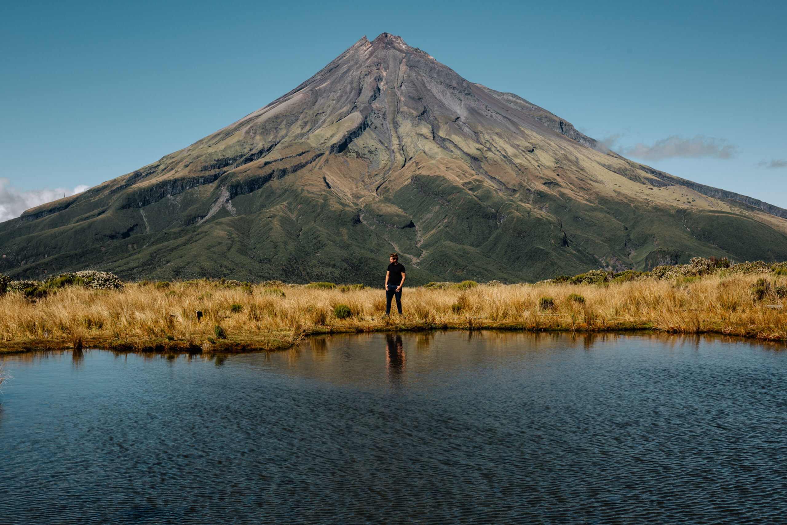 A  young male standing near the high mountain and a lake, Egmont National Park North New Zealand